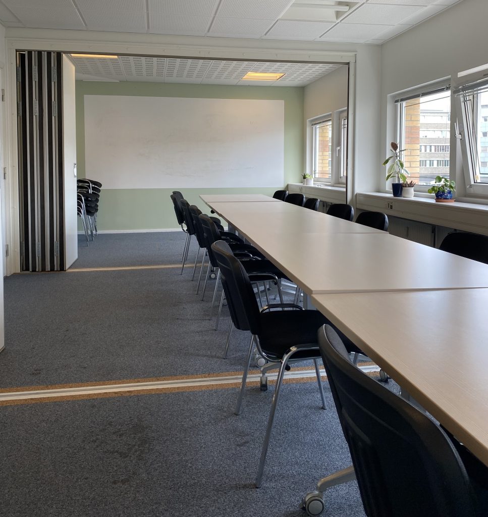 Mødelokale med whiteboard, tre mødeborde og 12 stole.